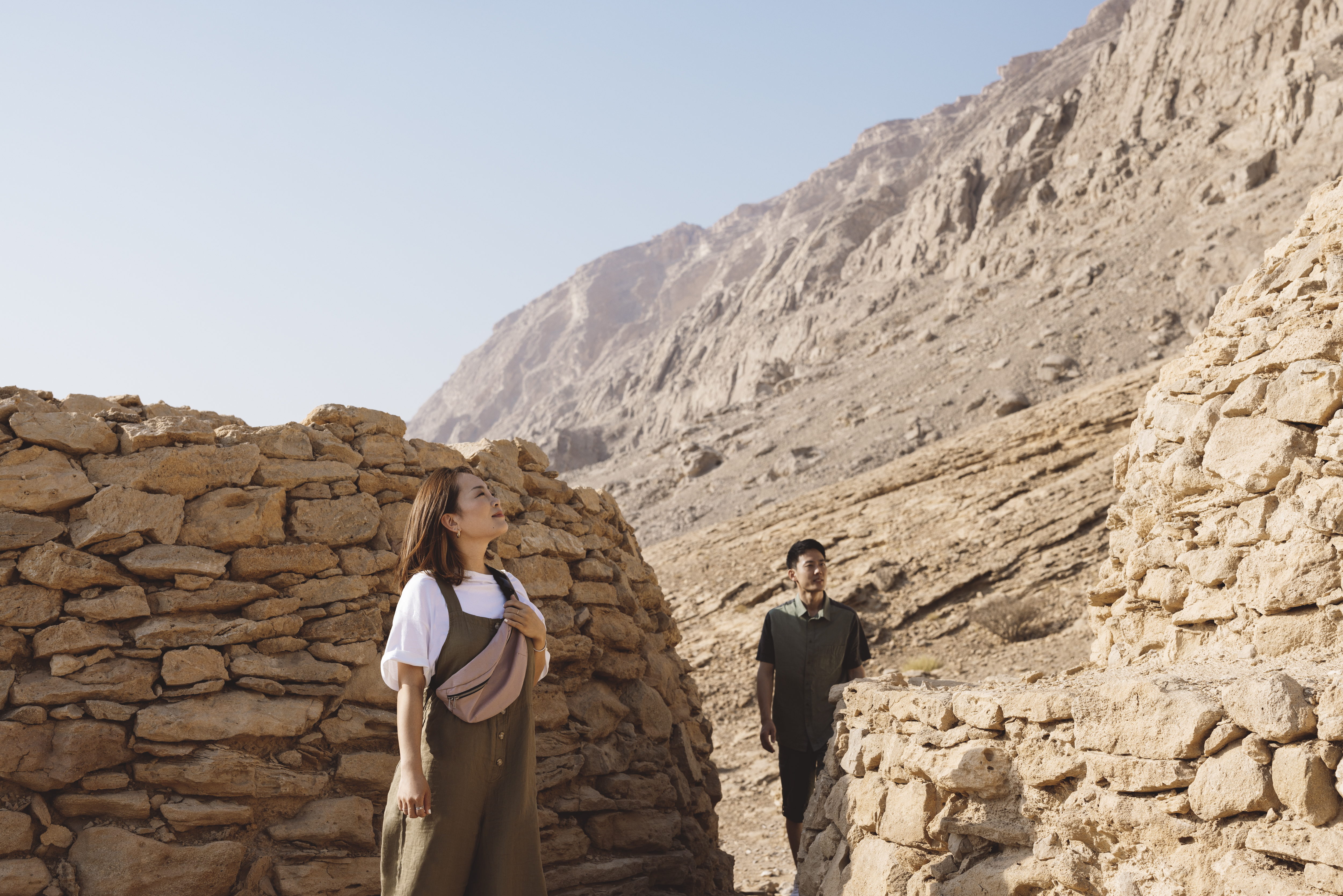 Couple exploring ancient stone tombs at Jebel Hafit in Al Ain, surrounded by rugged desert mountains.