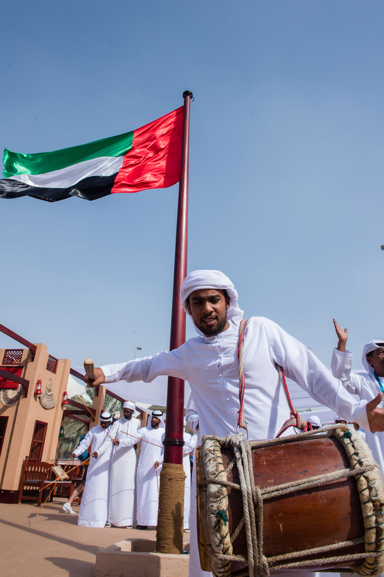 Emirati man playing traditional drum under UAE flag during cultural celebration in Abu Dhabi