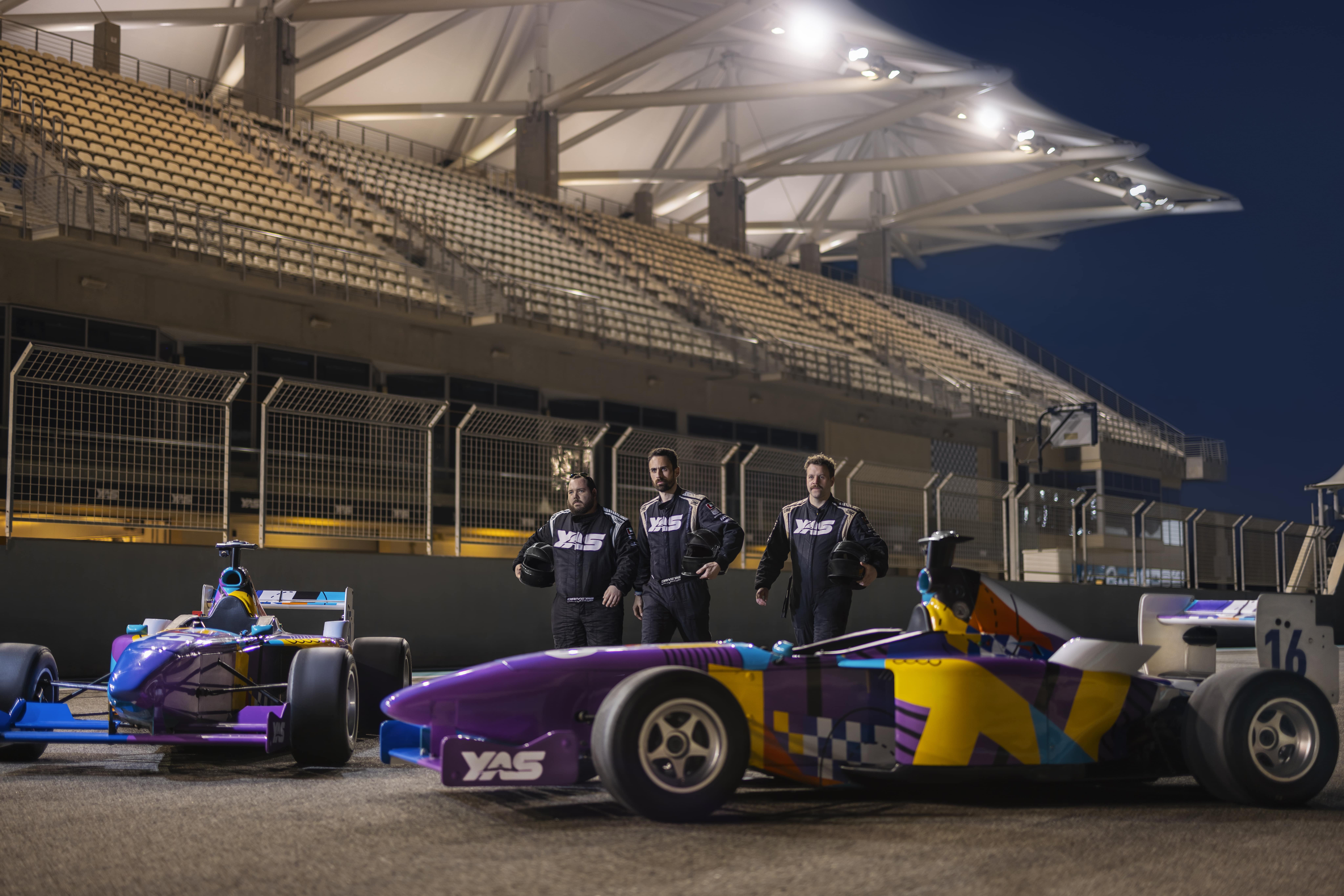 Race car drivers posing on track at Yas Marina Circuit under the lights of an empty grandstand