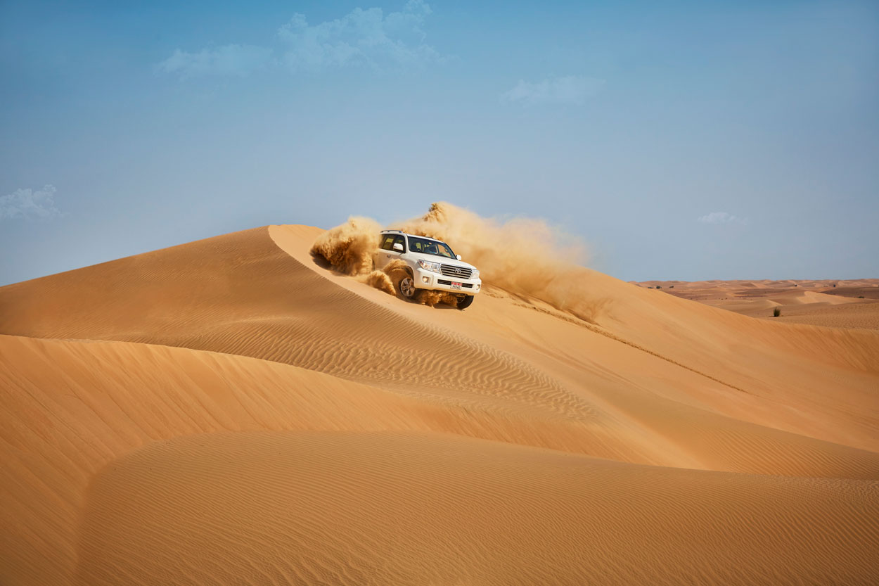 White 4x4 vehicle dune bashing through golden sand dunes in Abu Dhabi desert.