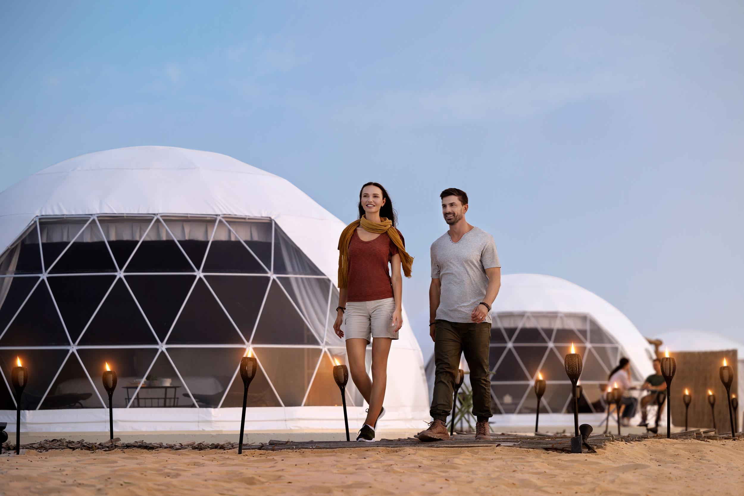 Couple walking outside luxury dome tents at a desert glamping site during sunset in Abu Dhabi.