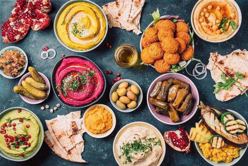 Colorful spread of Middle Eastern dishes including hummus, falafel, pickles, and fresh flatbread