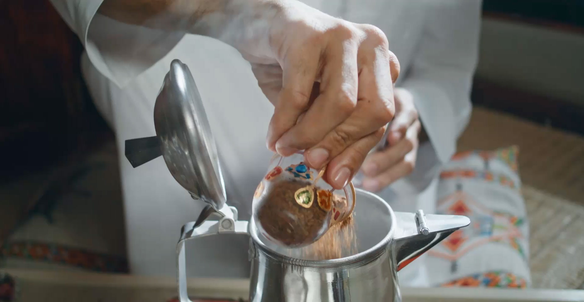 Hand adding traditional Arabic coffee grounds to a pot in a cultural setting