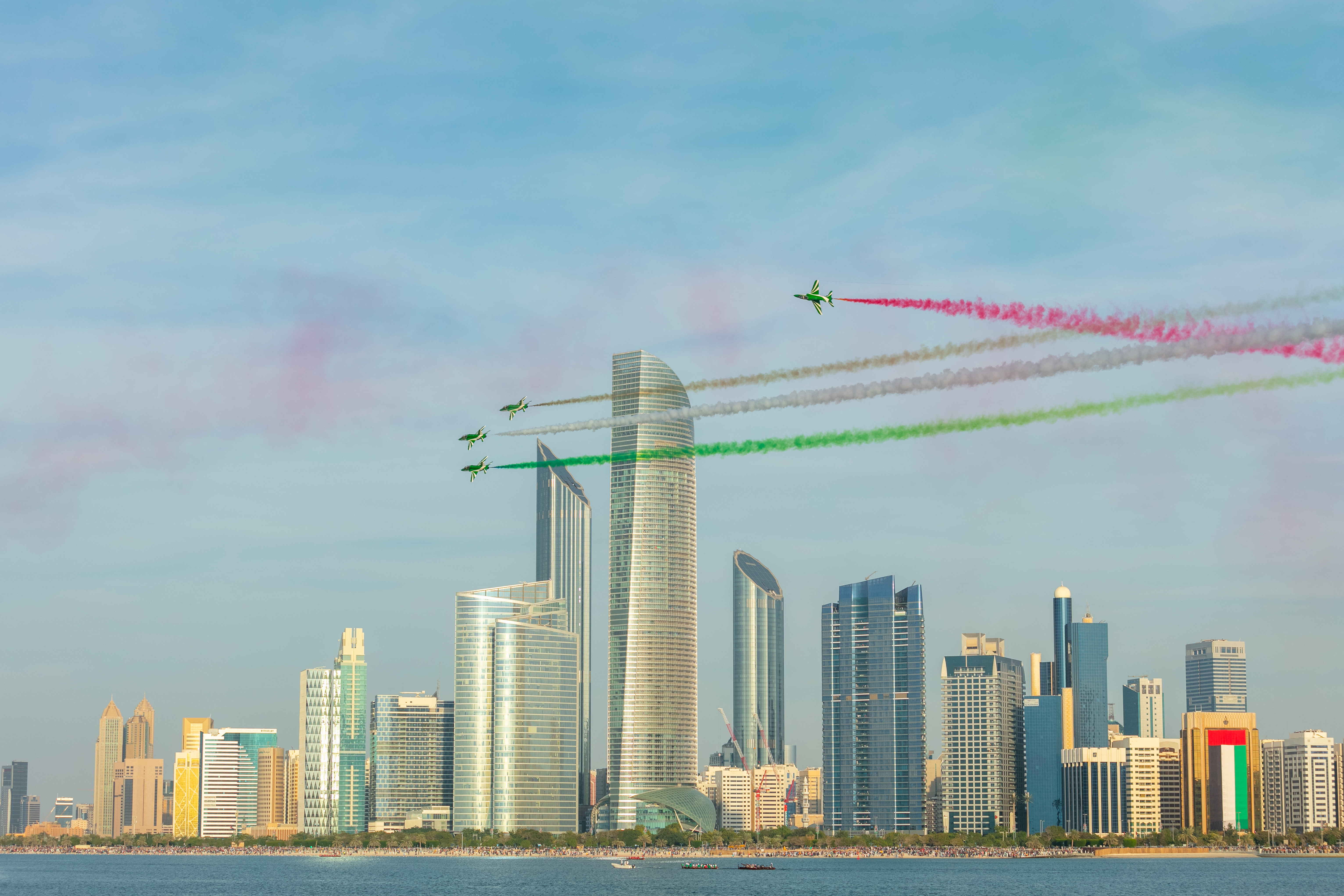 Airshow jets fly over Abu Dhabi skyline leaving UAE flag-colored smoke trails during National Day