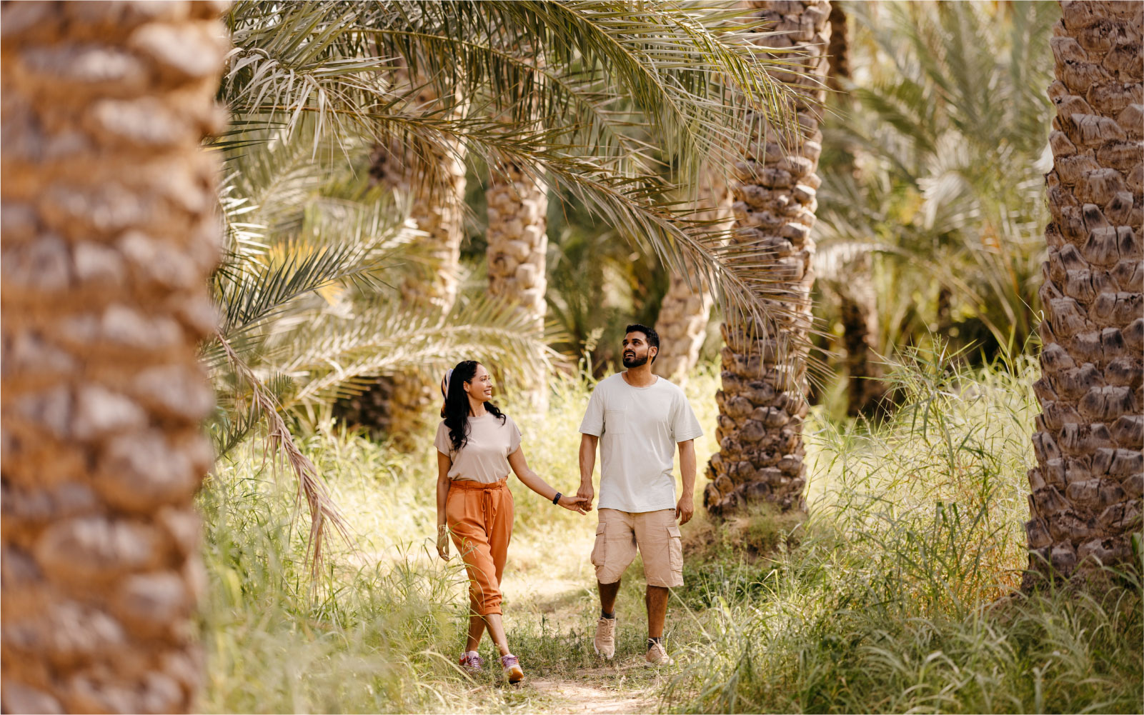 زوجان أجنبيان يتجولان وسط أشجار النخيل في إحدى واحات مدينة العين