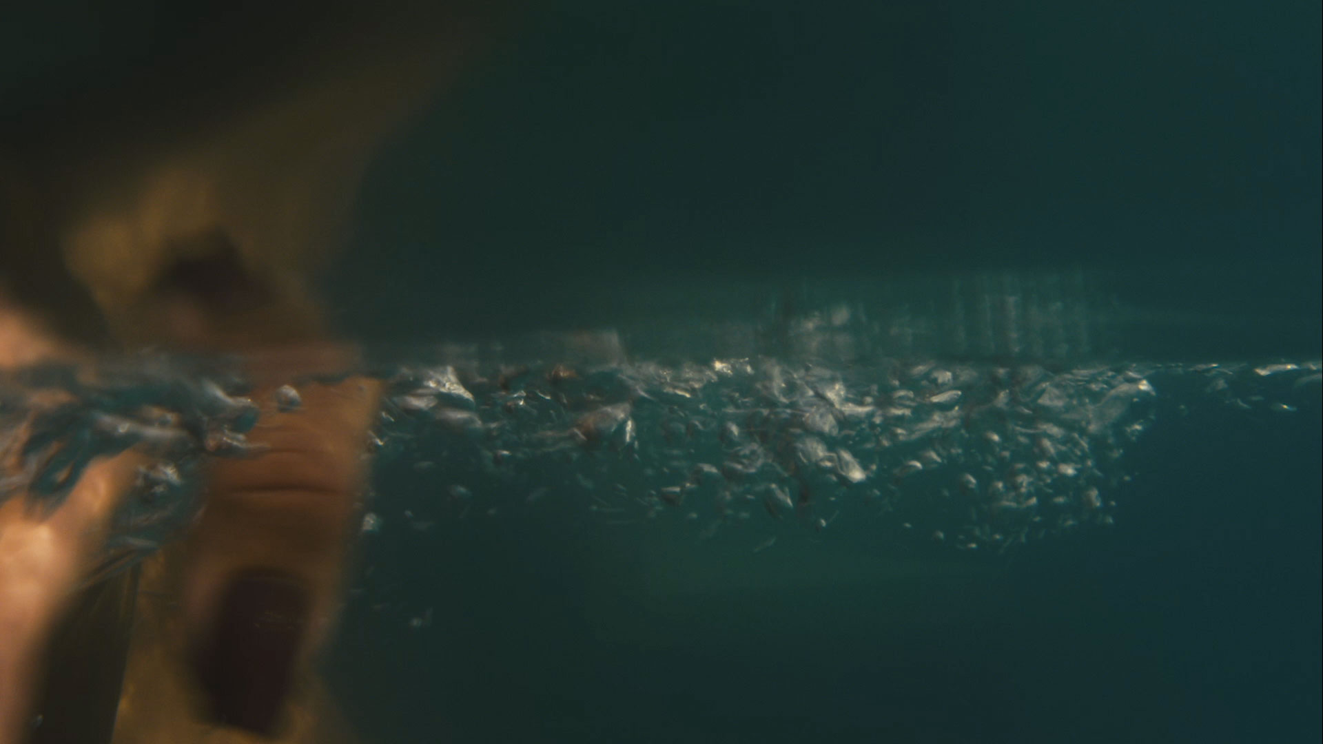 Underwater view with air bubbles and a blurred human face partially submerged.
