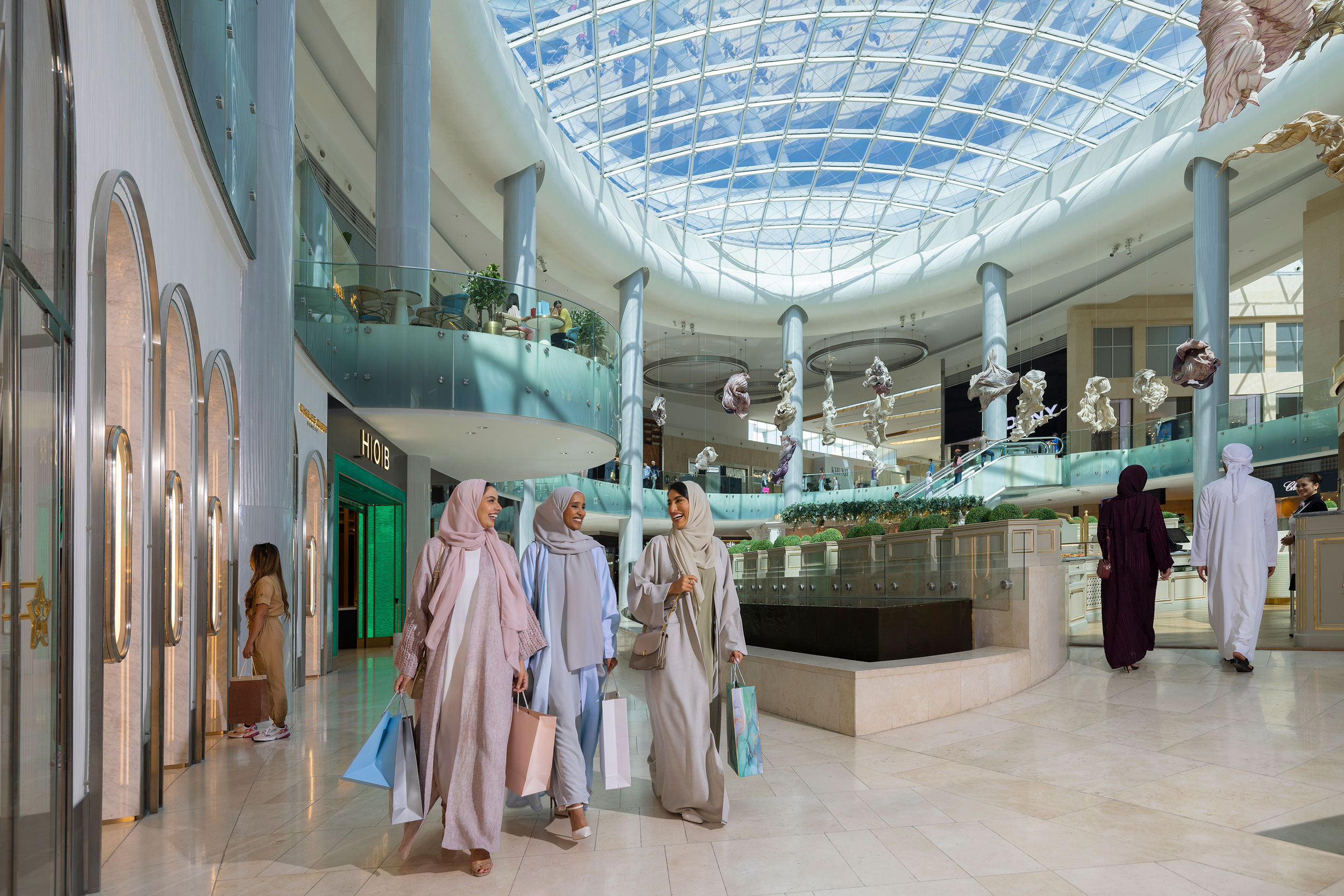 Three women enjoy shopping under a grand glass dome in an Abu Dhabi luxury mall.