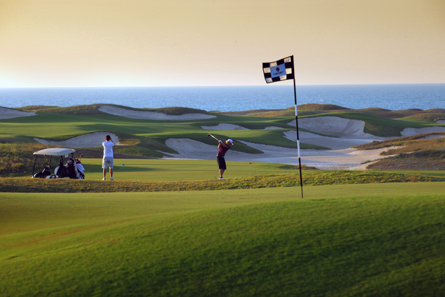 Two men playing golf near a golf cart at the Saadiyat Beach Golf Club in Abu Dhabi